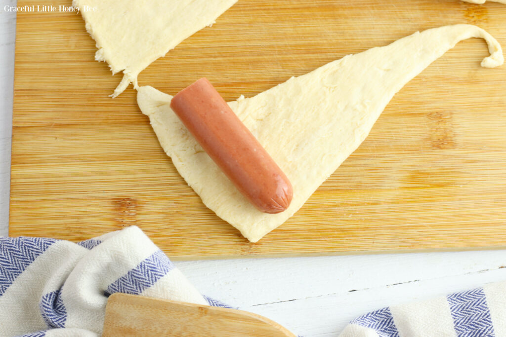 A triangle of crescent roll dough with a half piece of hot dog sitting on top.