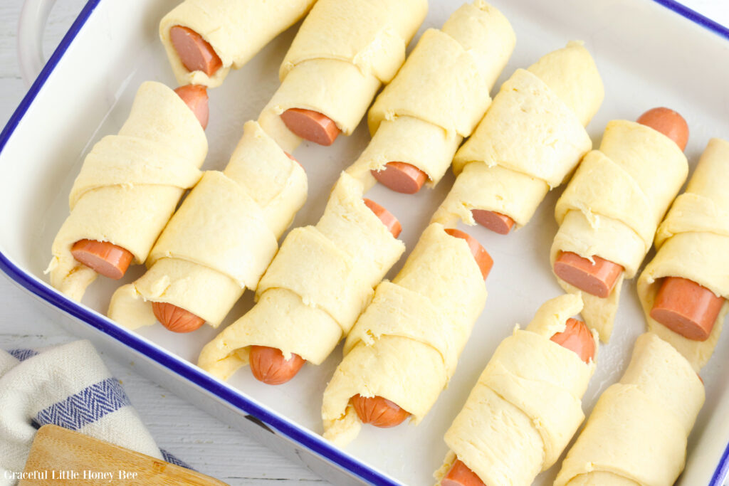 Hot dogs wrapped in crescent roll dough in a white casserole dish.