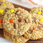 Monster Cookies sitting in a pile on a dark brown cutting board.