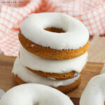 Stack of three donuts sitting on a wooden cutting board.