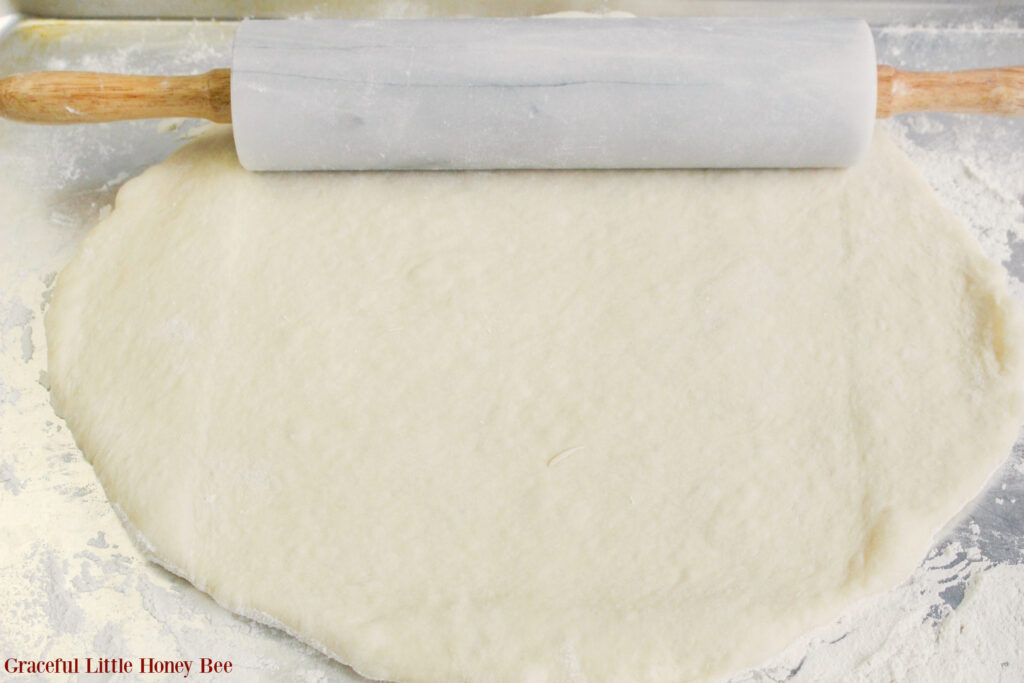 Dough rolled out on a marble counter with a rolling pin sitting next to it.