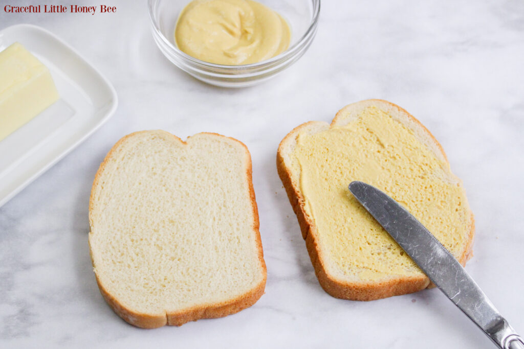 Dijon Mustard being spread on top of sandwich bread.