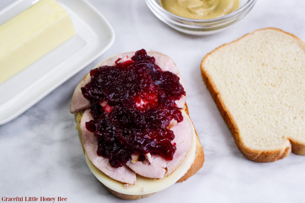 Open faced sandwich with mustard, cheese, turkey and cranberry sauce before being grilled.