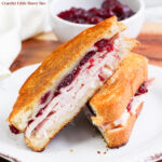 Turkey Cranberry Grilled Cheese sliced in half and laying on a white plate.