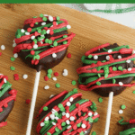 Chocolate covered Ritz Pops sitting on a wooden cutting board.