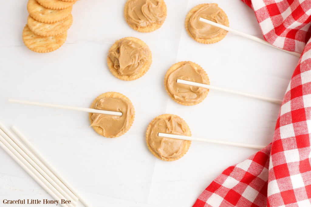 Ritz crackers with a layer of peanut butter on top and a sucker stick sitting in the peanut butter of each cracker.