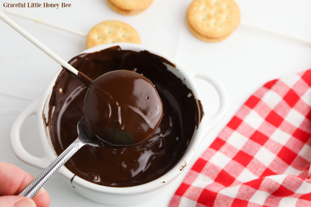 A Ritz Pop covered in chocolate coming up out of the chocolate sauce.