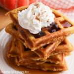 A stack of pumpkin waffles with whipped cream on top.