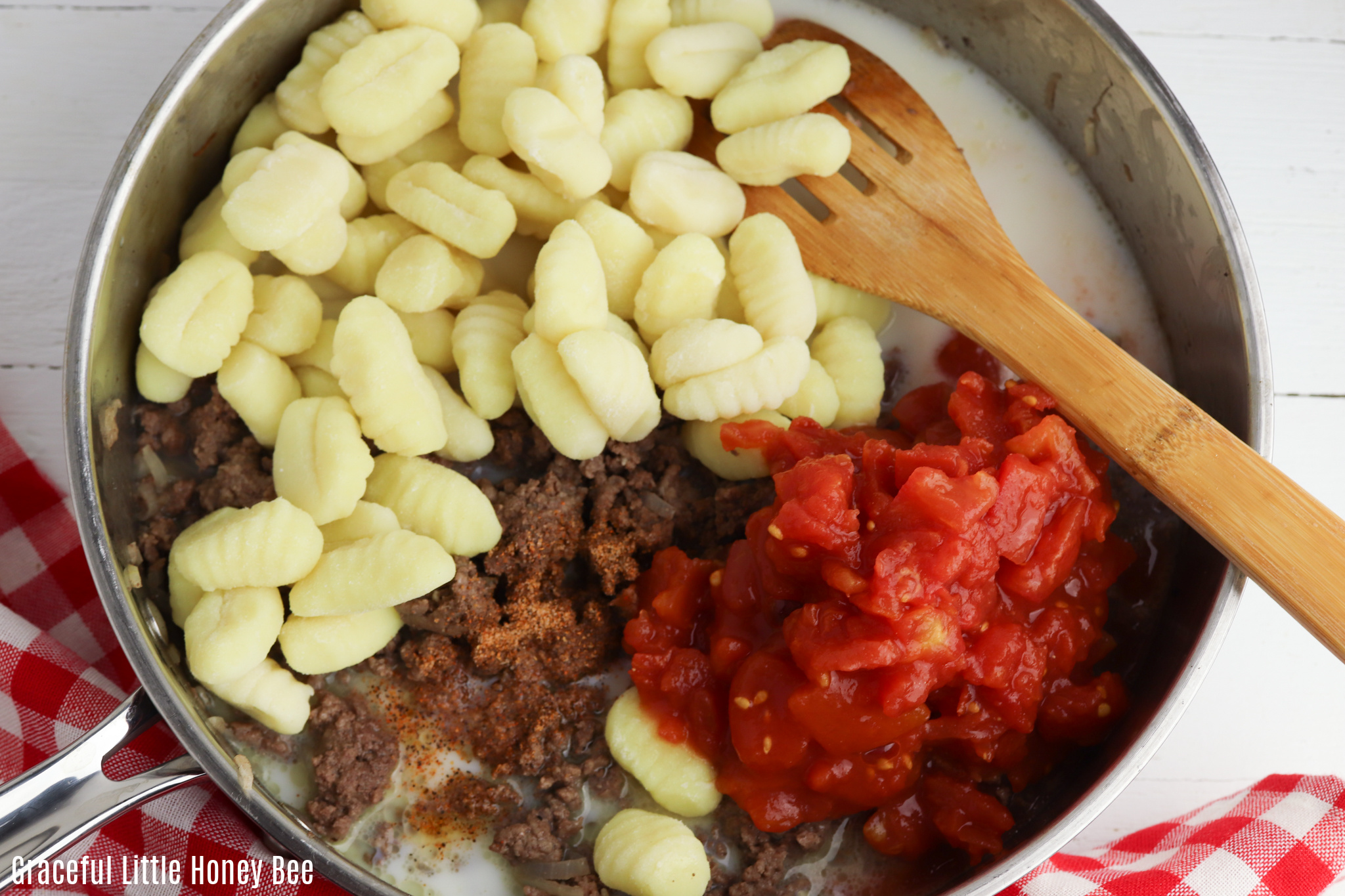 Uncooked gnocchi, diced tomatoes and cooked beef in pan before being stirred together.