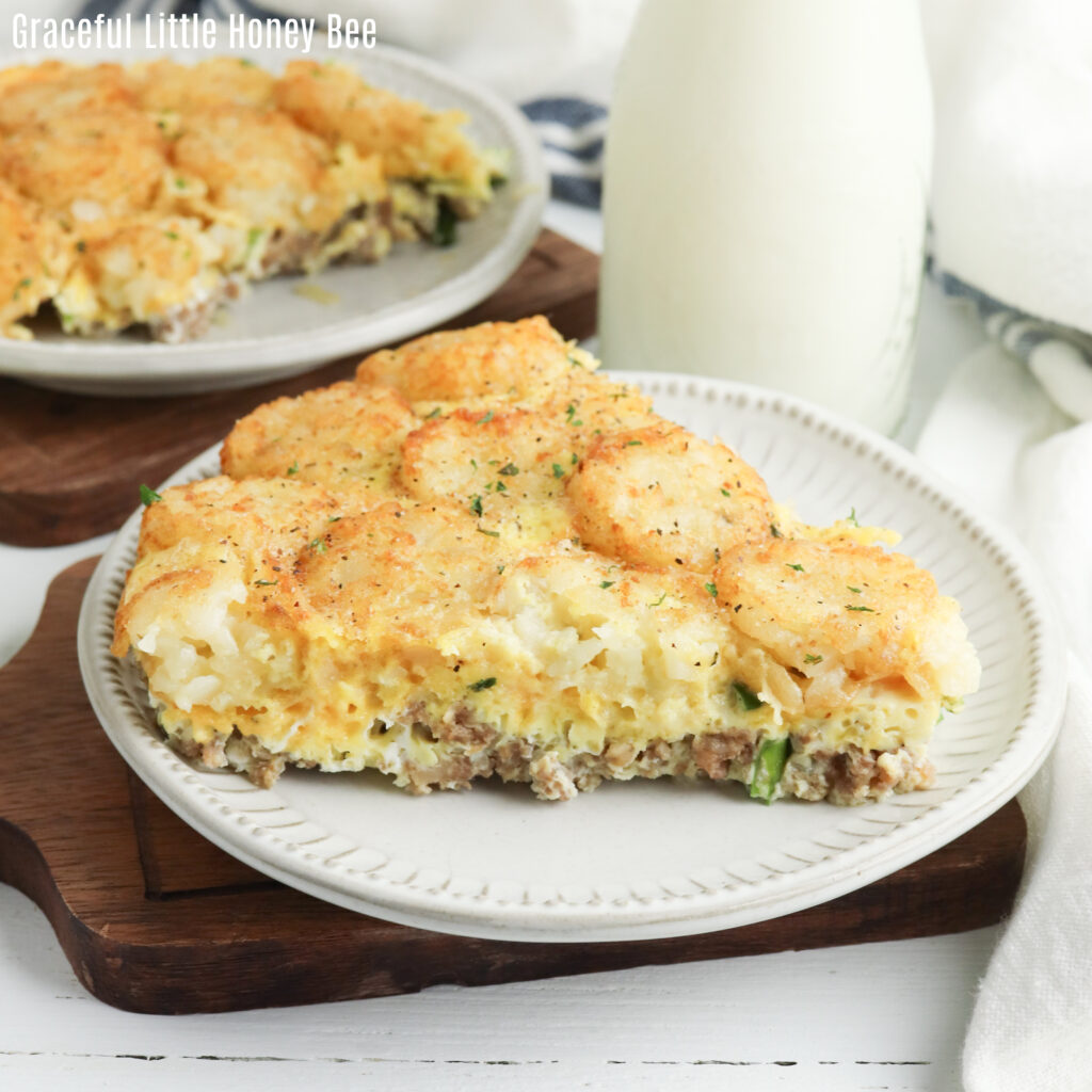 A slice of tater tot breakfast casserole sitting on a white plate with a glass of milk in the background.