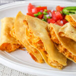 Close up of a crispy, buttery chicken quesadilla sitting on a white plate garnished with jalapenos and fresh salsa.