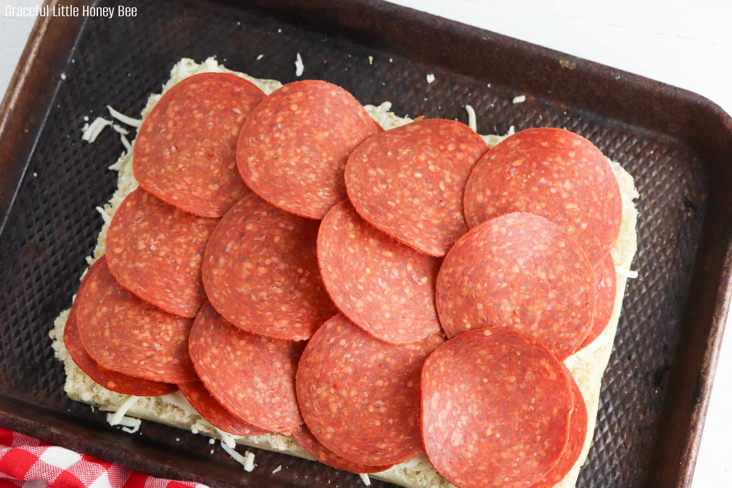 Bottom slab of rolls sitting on a baking sheet sprinkled with mozzarella cheese and a layer of pepperoni slices.