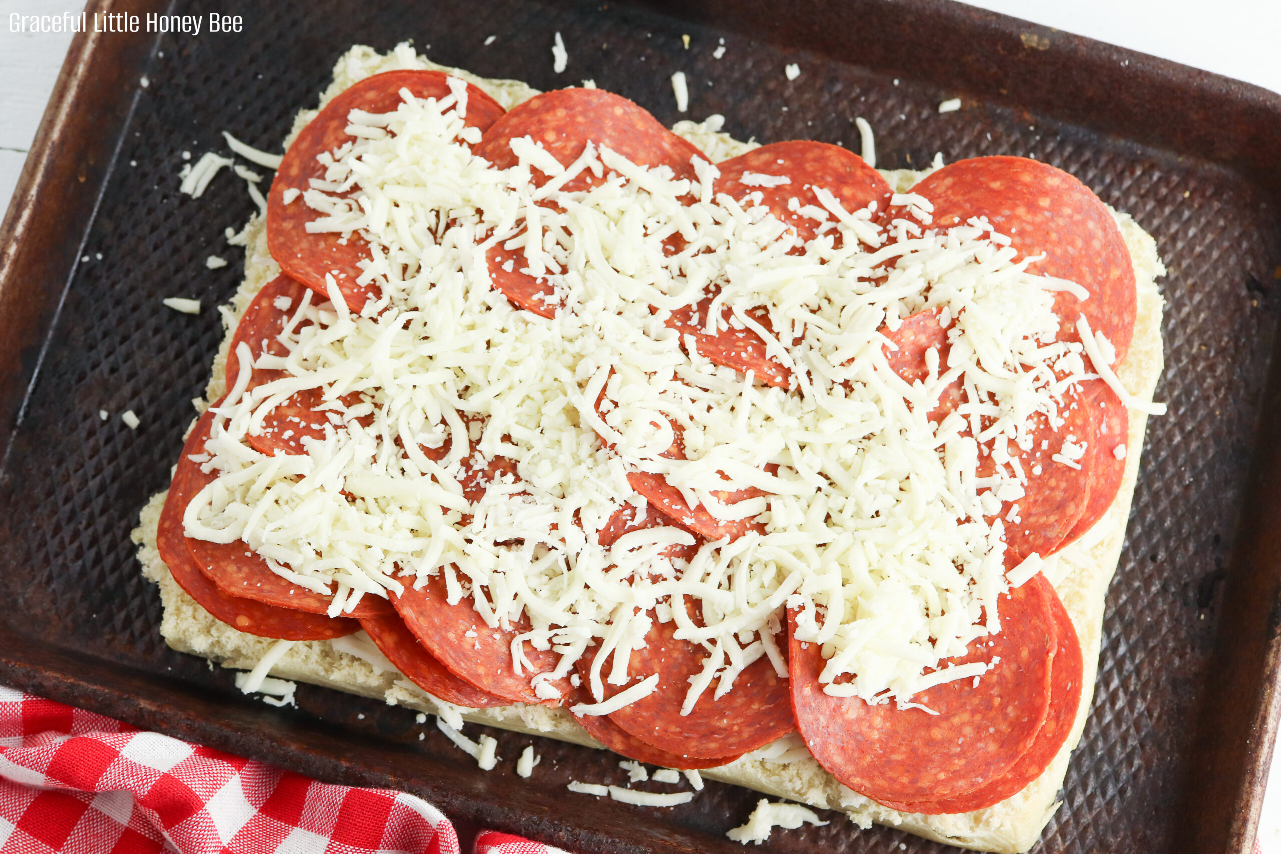 Bottom slab of rolls sitting on a baking sheet sprinkled with mozzarella cheese, a layer of pepperoni slices and topped with more mozzarella cheese.