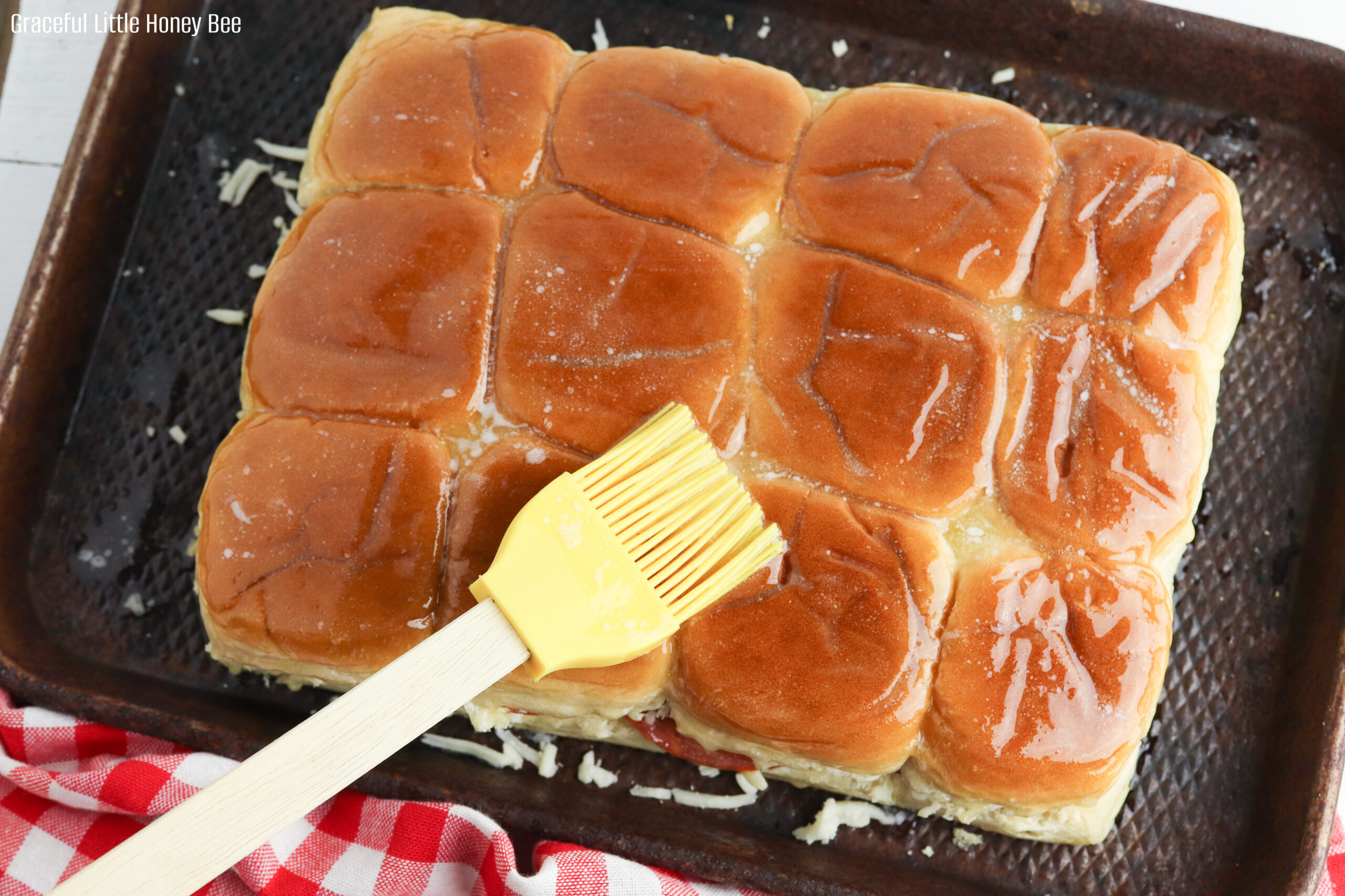Sliders sitting on a baking sheet and slathered with butter.