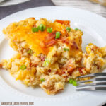 A serving of Loaded Baked Potato Casserole sitting on a round white plate with a fork.