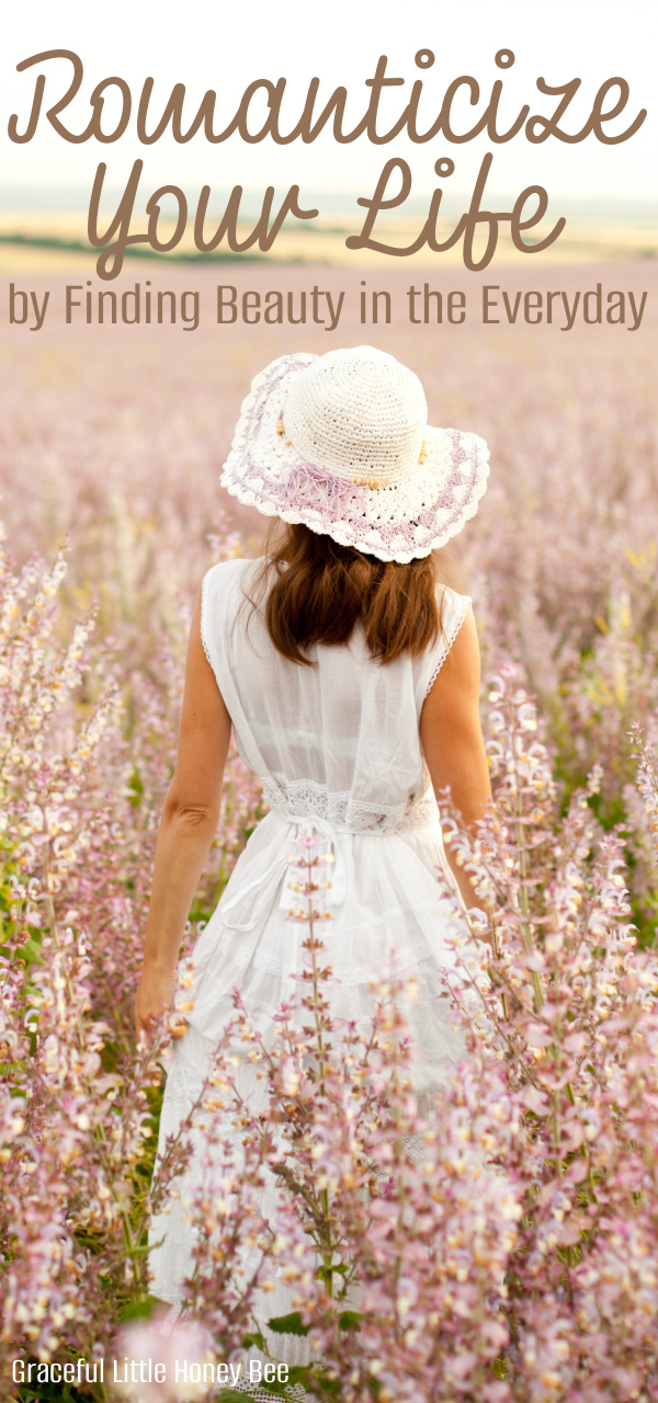 A woman standing in a flower field wearing a white lace dress and dainty white hat.