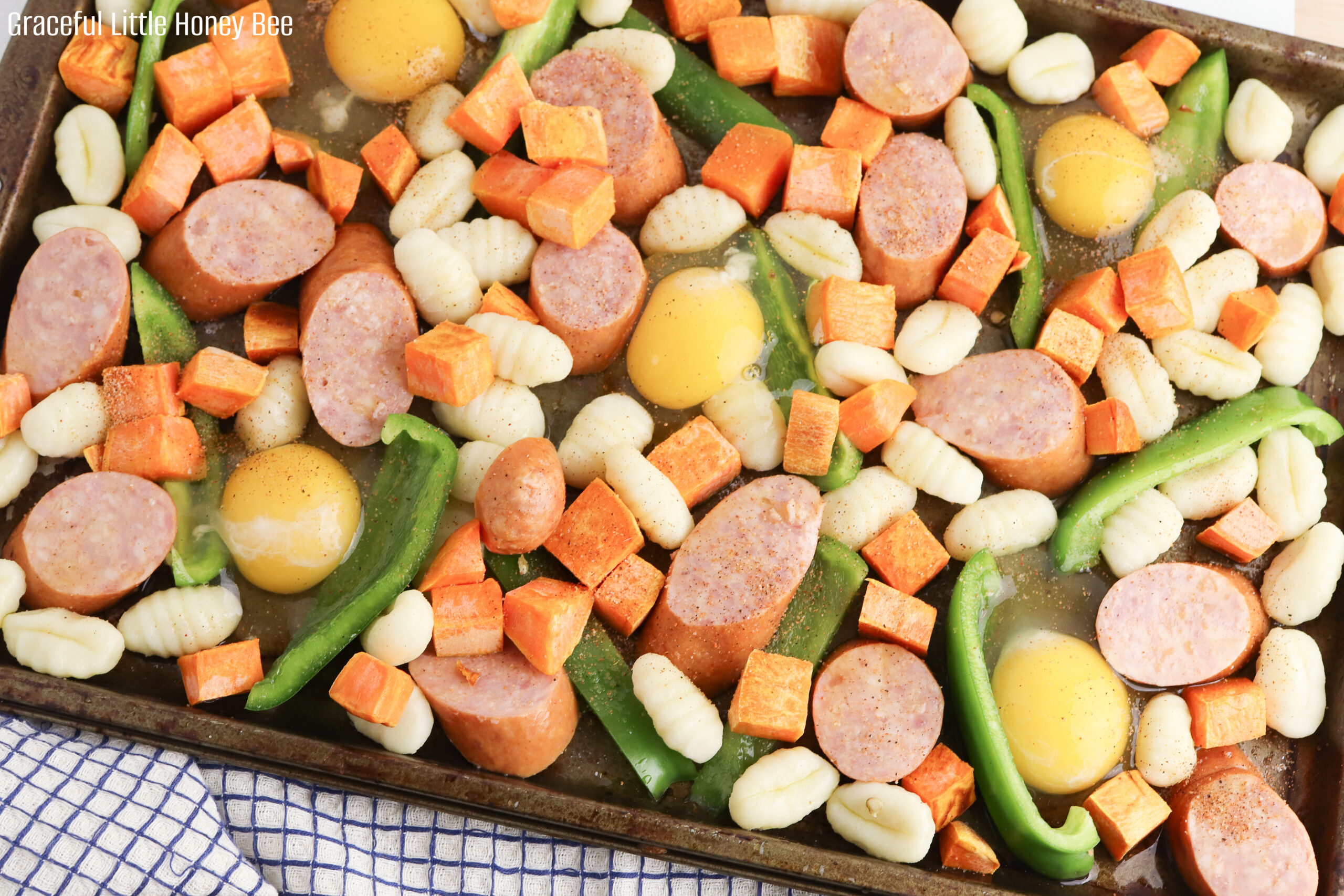 Diced sweet potatoes, sliced bell pepper, sliced sausage, gnocchi and egg sitting on a baking sheet before going into the oven.