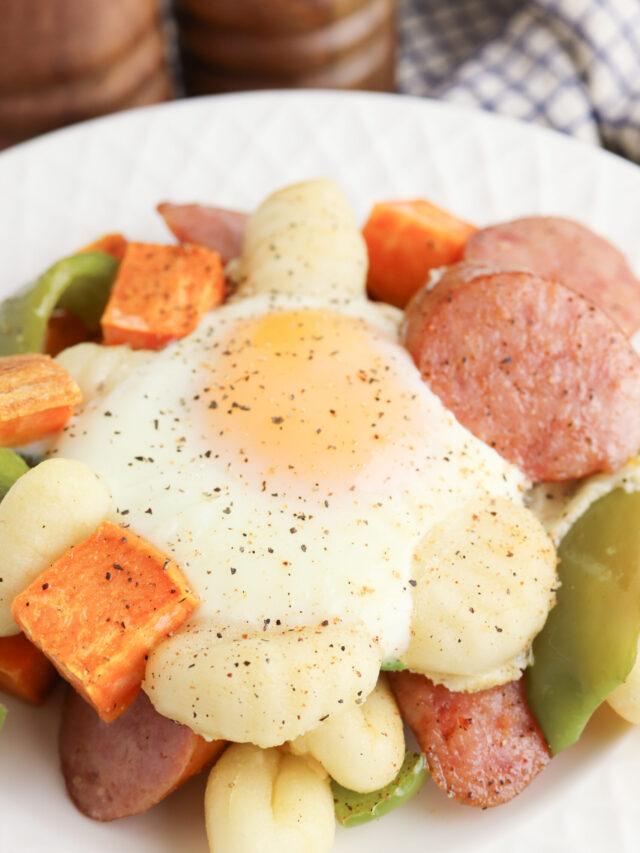 A serving of Sausage, Egg and Gnocchi sitting on a round, white plate.