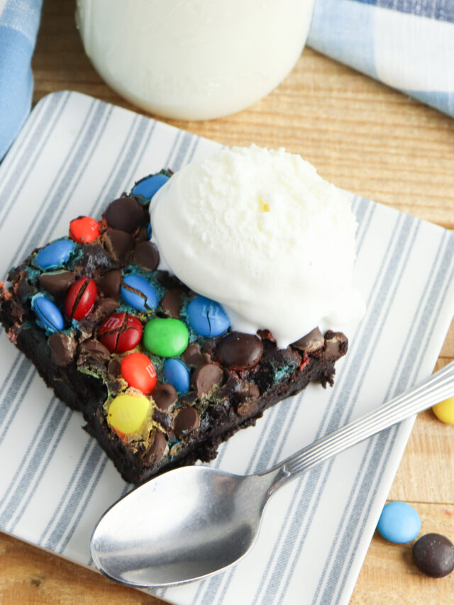 A serving of chocolate dump cake sitting on a blue and white striped plastic plate with a scoop of vanilla ice cream on top.