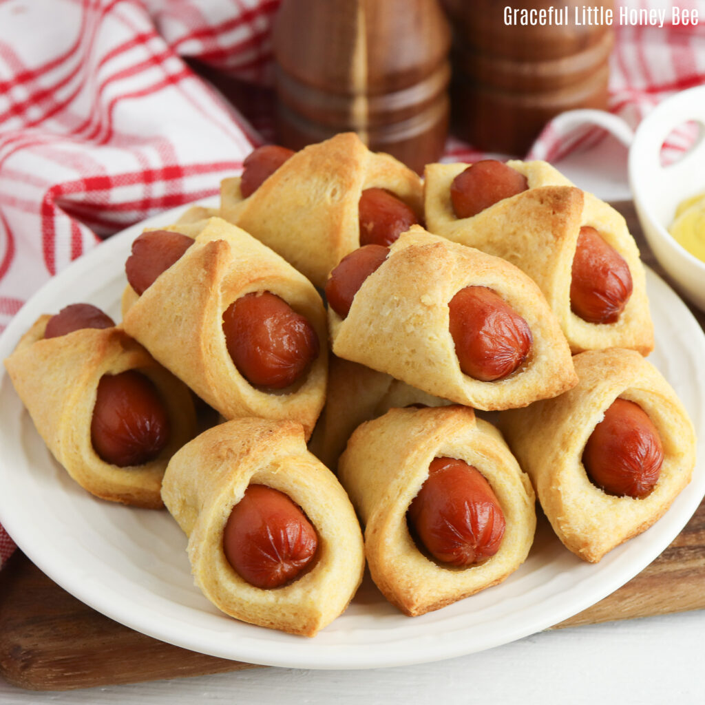 Corn dog pigs in a blanker sitting in a pile on a white plate.