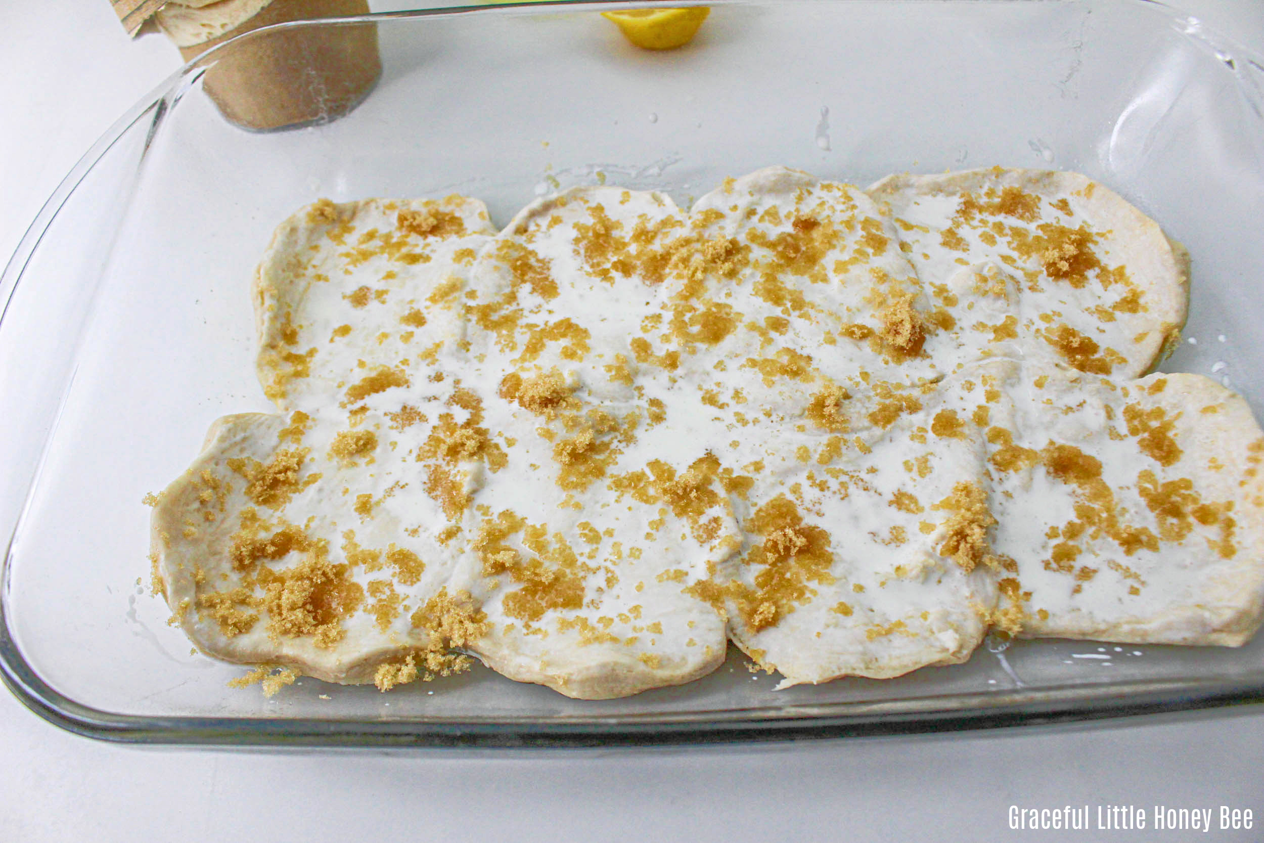 Raw biscuits in baking dish with cream and brown sugar on top.