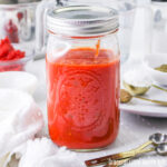 Spaghetti sauce in a mason jar with metal teaspoons sitting next to it.