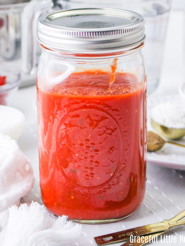 Spaghetti sauce in a mason jar with metal teaspoons sitting next to it.