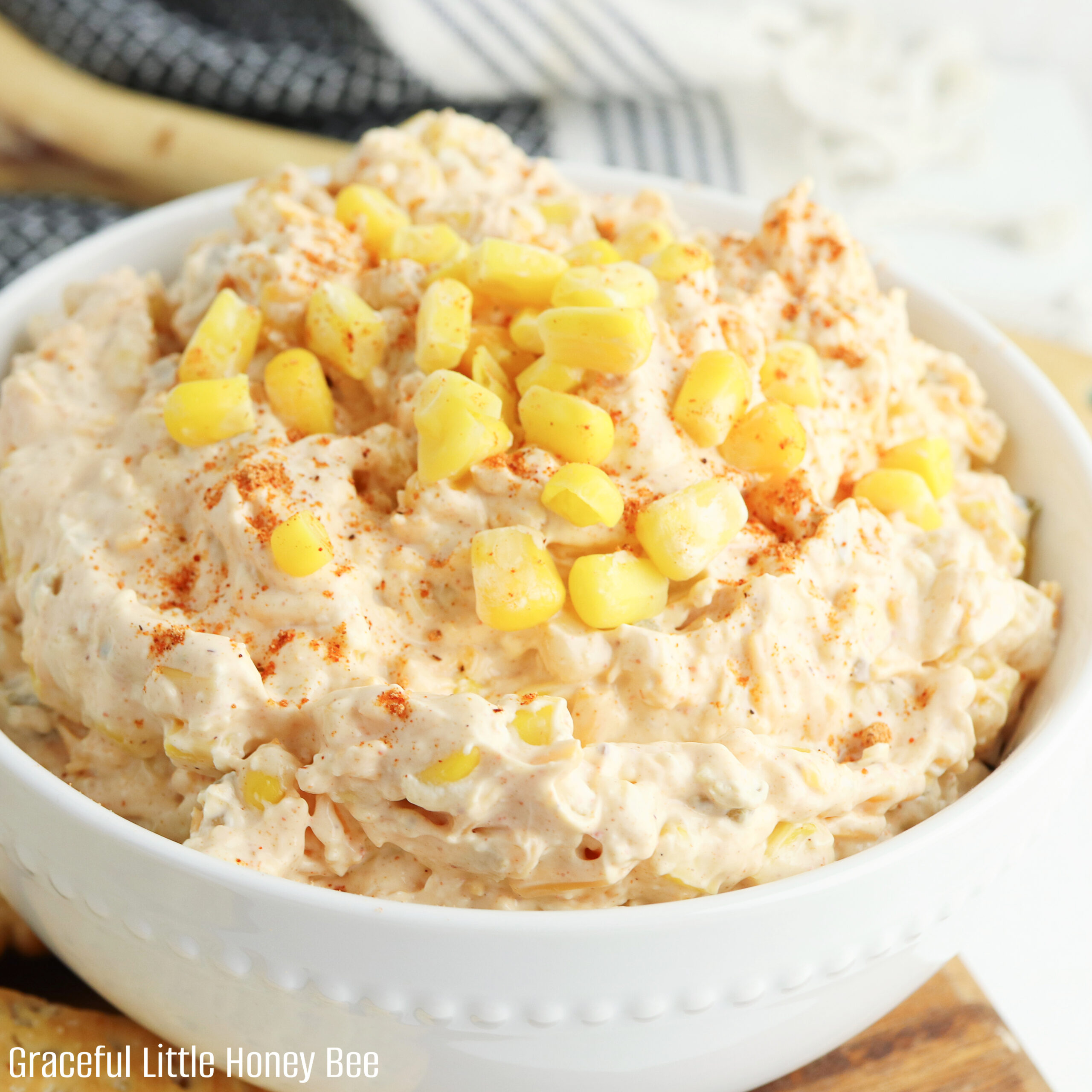 A close up view of corn dip with corn kernels on top for garnish in a white bowl.