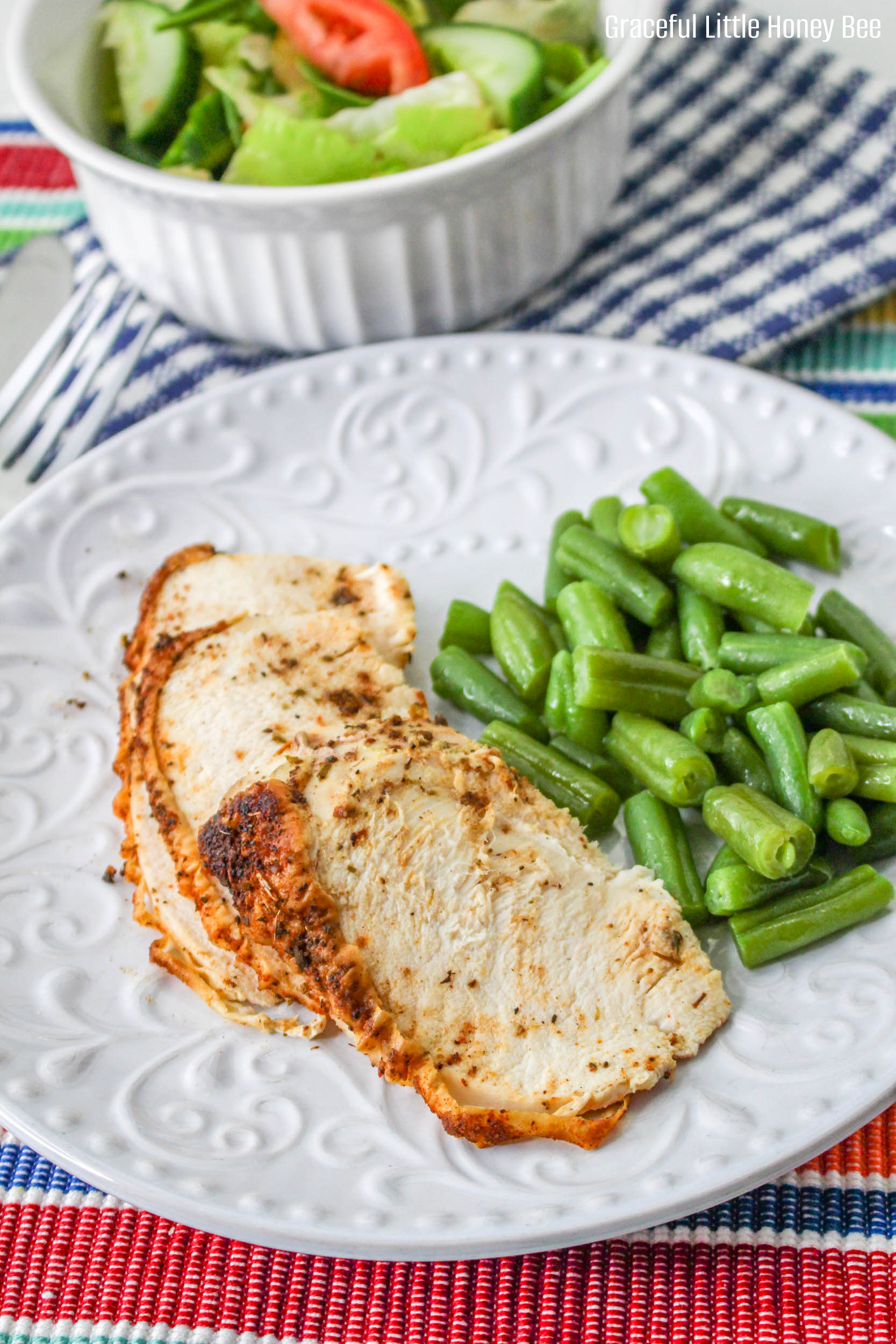 Air fried chicken breast slices sitting on a white plate with green beans.