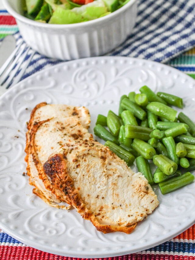 Air fried chicken breast slices sitting on a white plate with green beans.