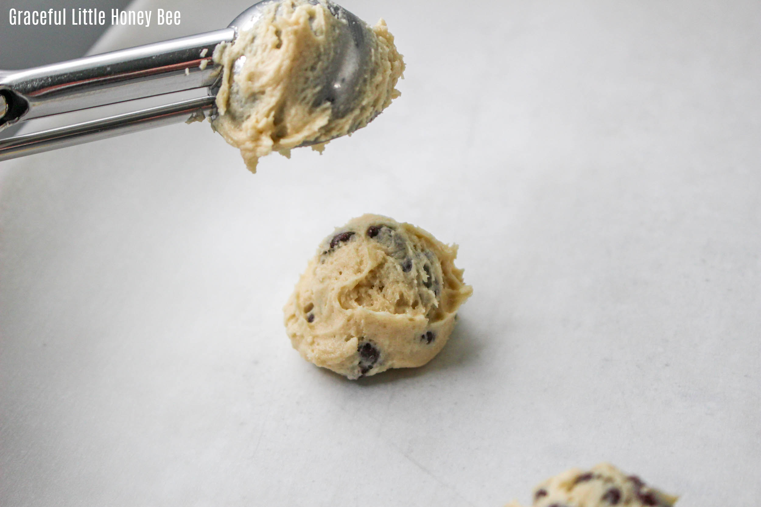 Cookie dough being put on parchment paper with a dough scoop.