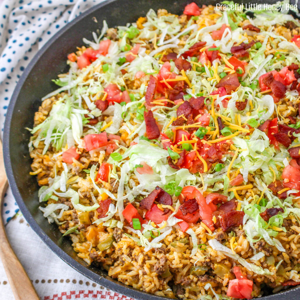 Cheeseburger Fried Rice topped with shredded lettuce, bacon and diced tomatoes in a cast iron skillet.