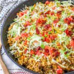 Cheeseburger Fried Rice topped with shredded lettuce, bacon and diced tomatoes in a cast iron skillet.