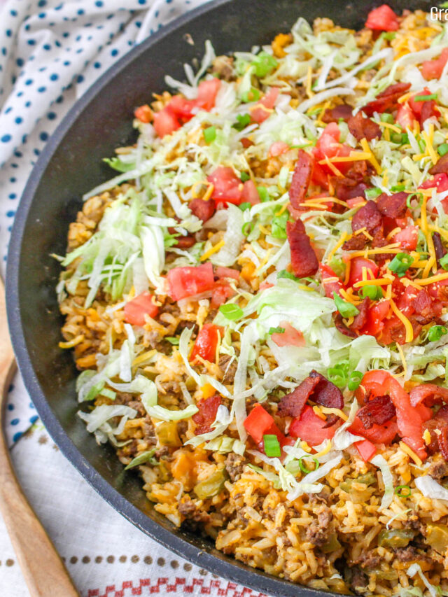 Cheeseburger Fried Rice topped with shredded lettuce, bacon and diced tomatoes in a cast iron skillet.