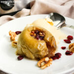 A close up view of a stuffed apple on a white plate with vanilla ice cream.