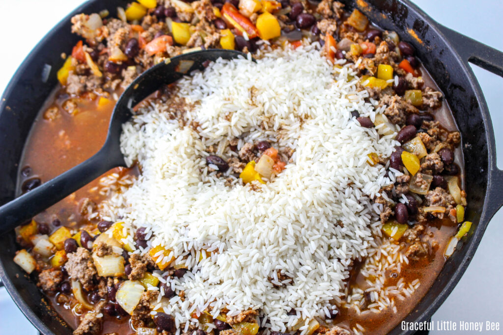 Uncooked rice on top of beef mixture in skillet.