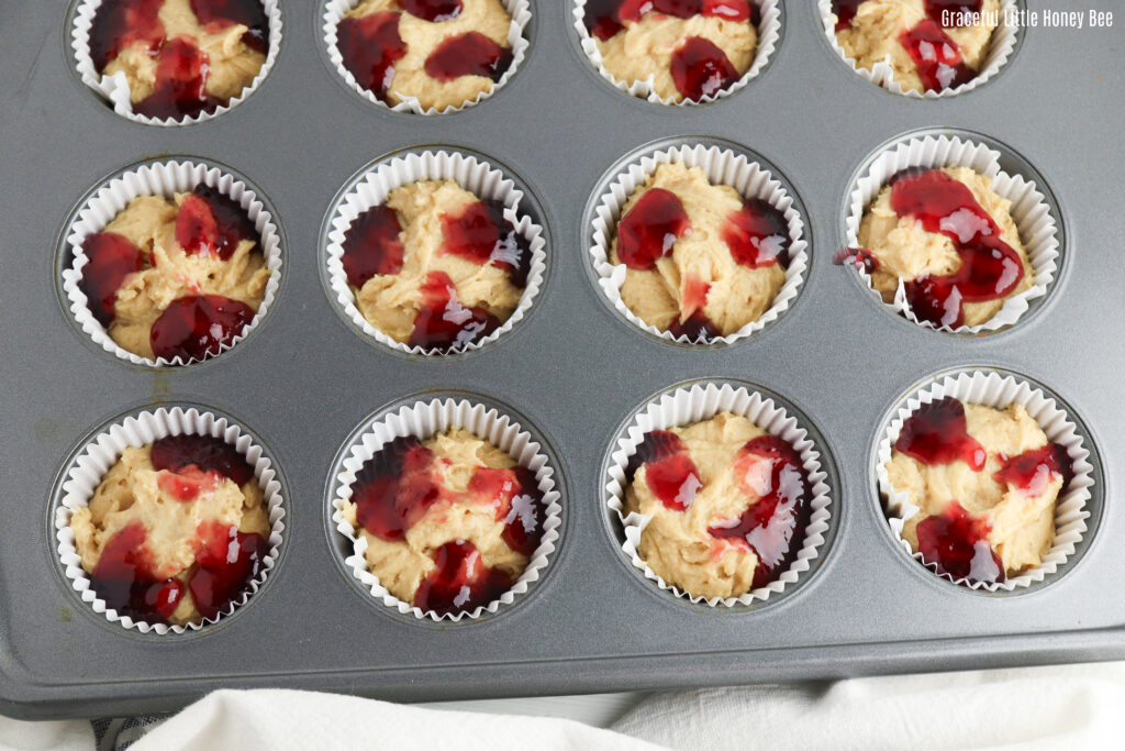 Peanut butter muffins topped with jelly in a muffin tin.