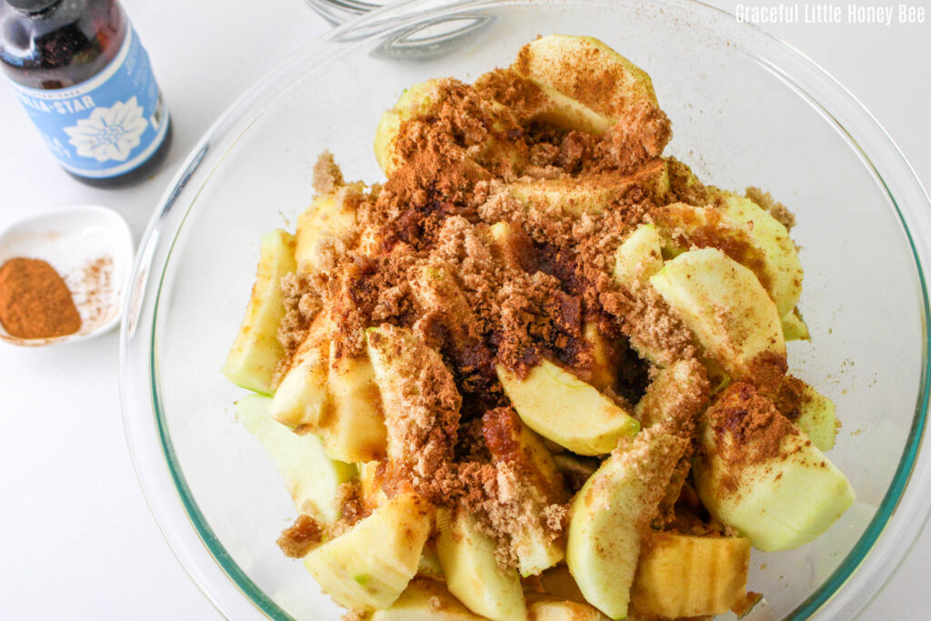 Peel and sliced apples topped with cinnamon in a clear glass mixing bowl.