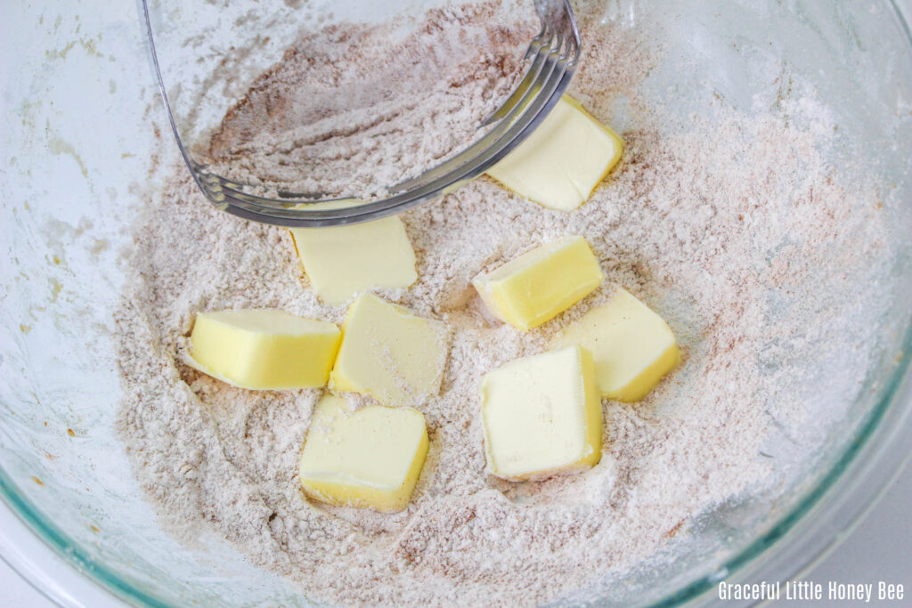 Dry ingredients and pats of butter in a clear mixing bowl with a pastry cutter.