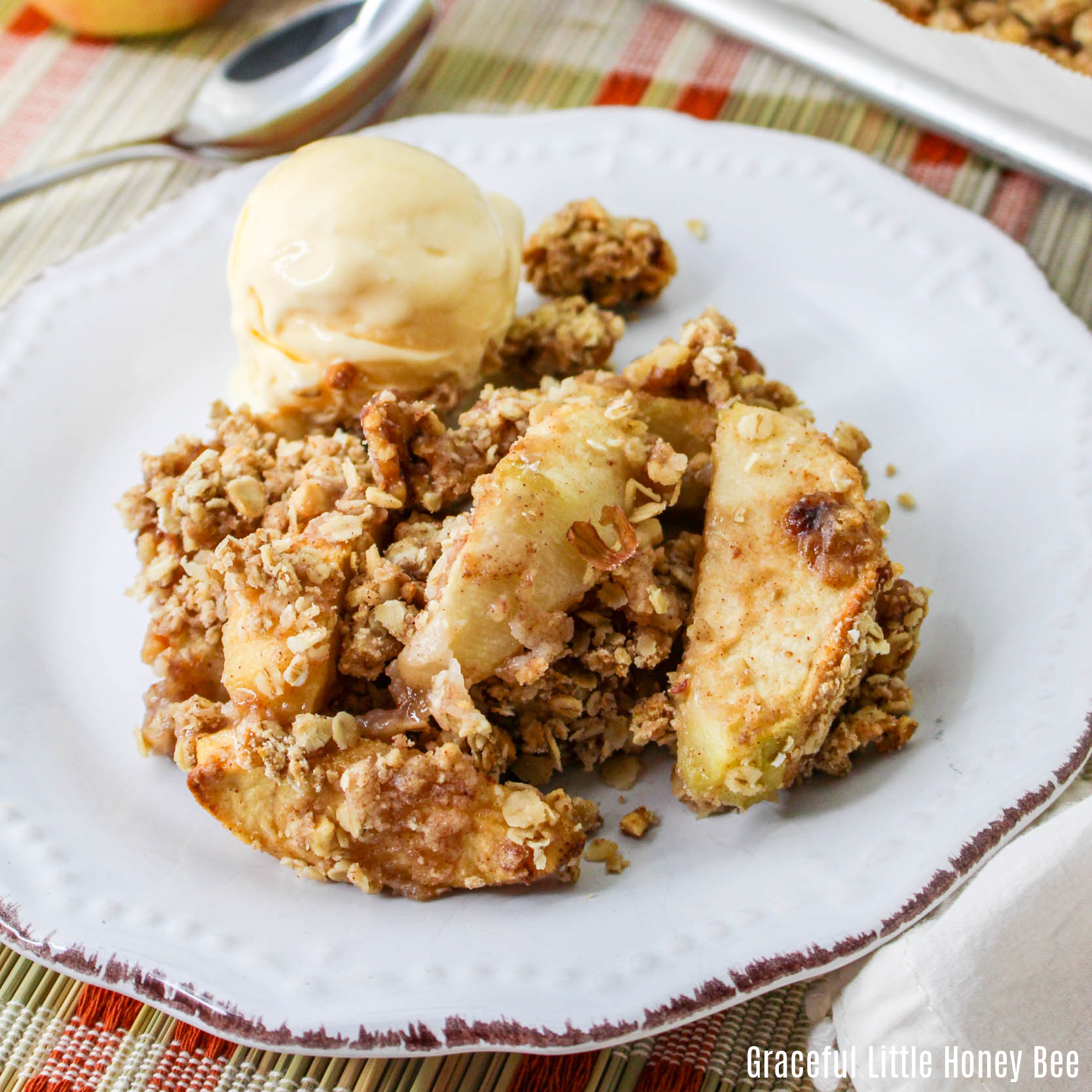 A serving of sheet pan apple crisp with vanilla ice cream on a white, round plate.