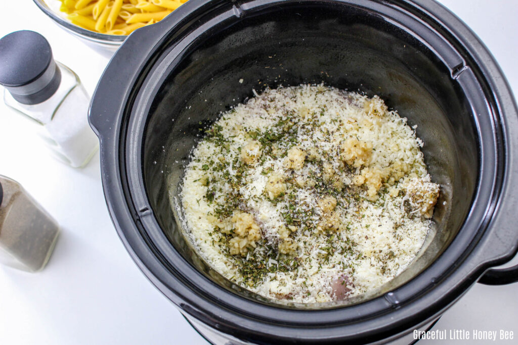 All ingredients for Parmesan Garlic Chicken in a small, round black slow cooker before cooking.