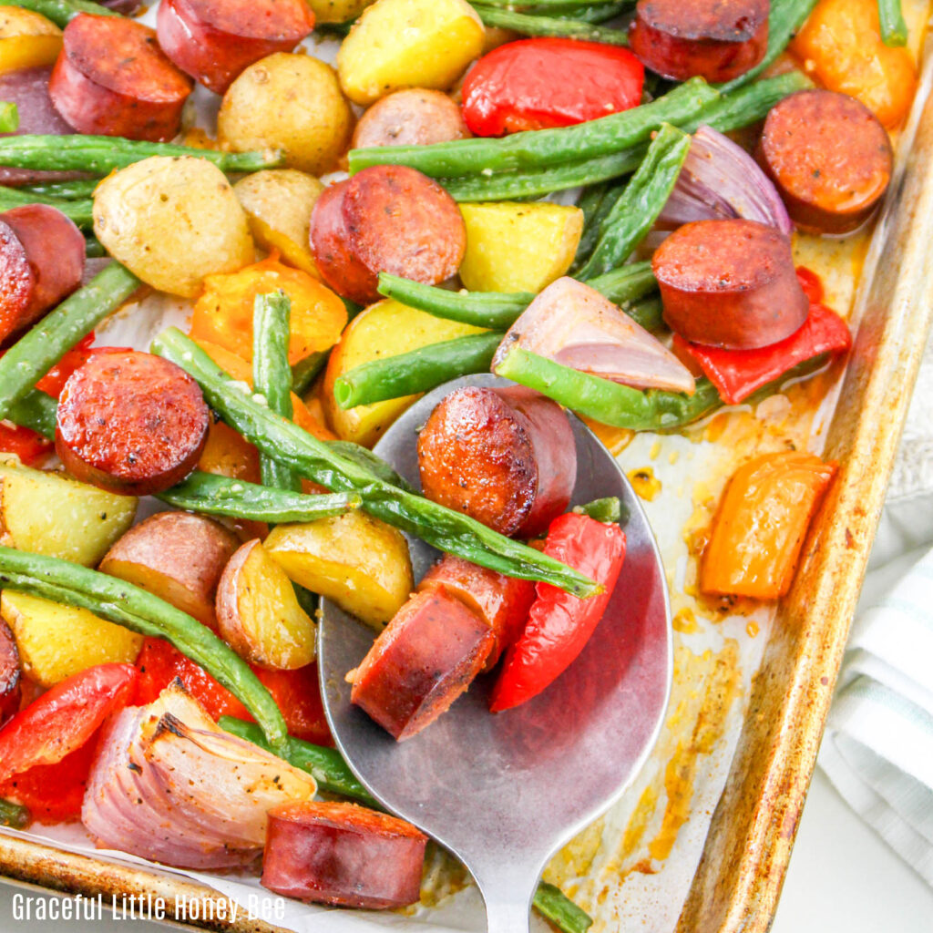 Close up view of sausage sheet pan dinner with a silver serving spoon.