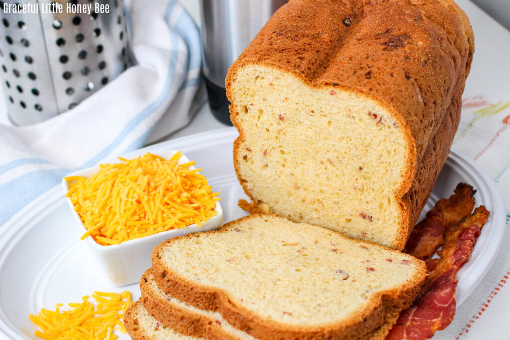 Bacon Cheddar Bread sliced on a cutting board with shredded cheese.