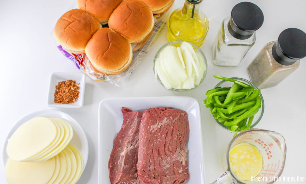 An aerial view of slider buns, steak, cheese, peppers, onions and seasonings sitting on a countertop.