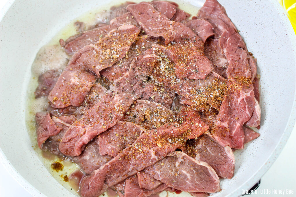 Sliced steak being sauteed in a pan.