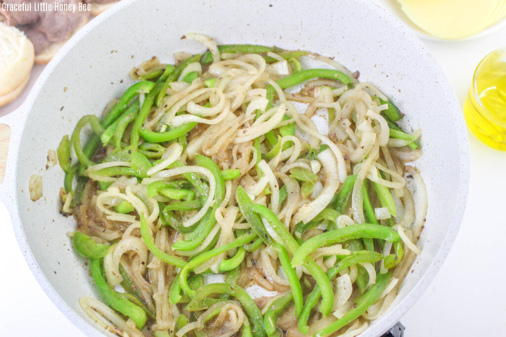 Sliced peppers and onions being sauteed in a pan.