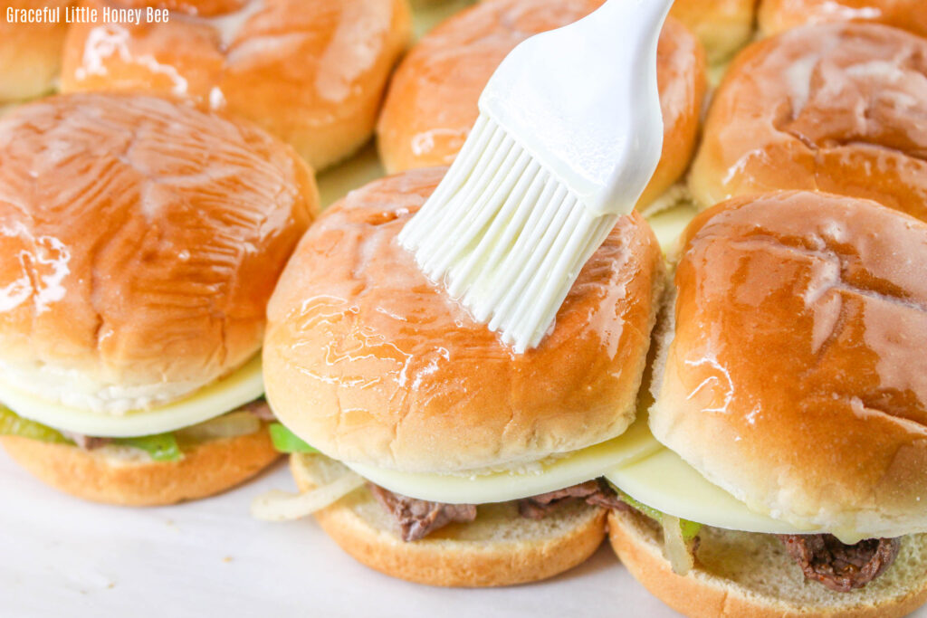 Slider bun tops being brushed with melted butter.