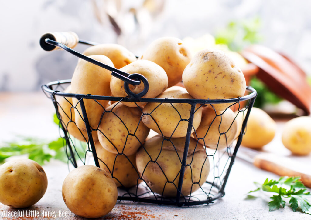 Potatoes in a black wire basket, sitting on a countertop with vegetables in the background.