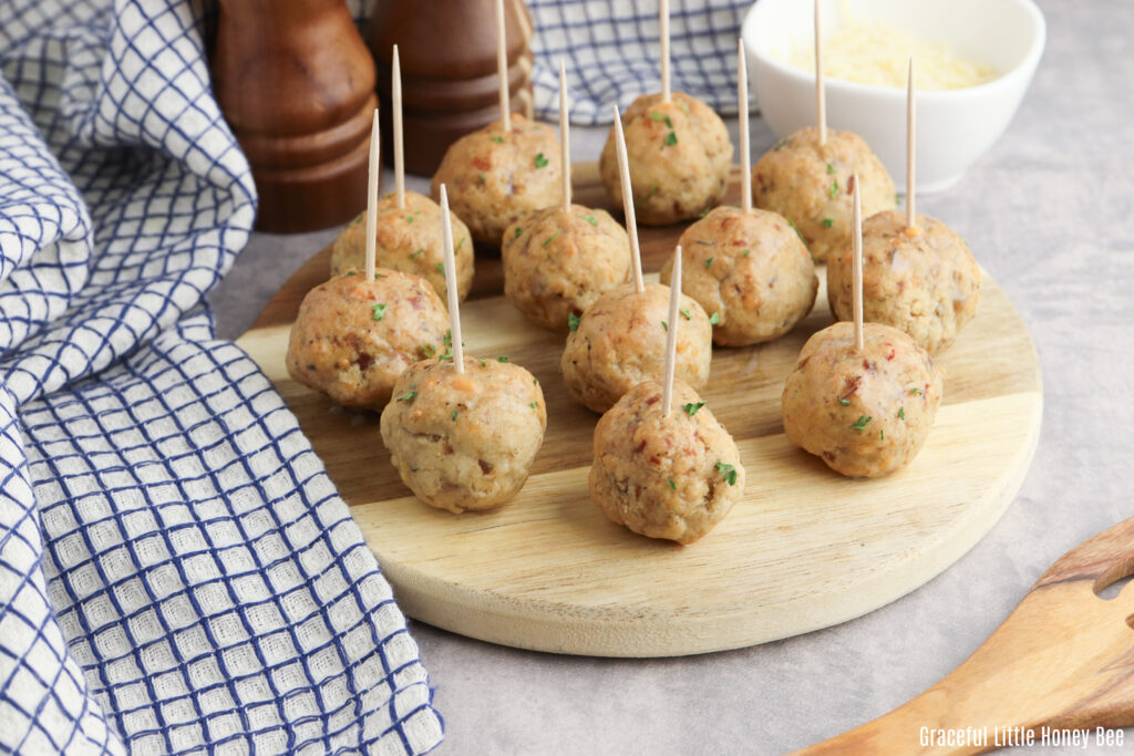 Sausage balls with toothpicks in them on a round wooden plate.