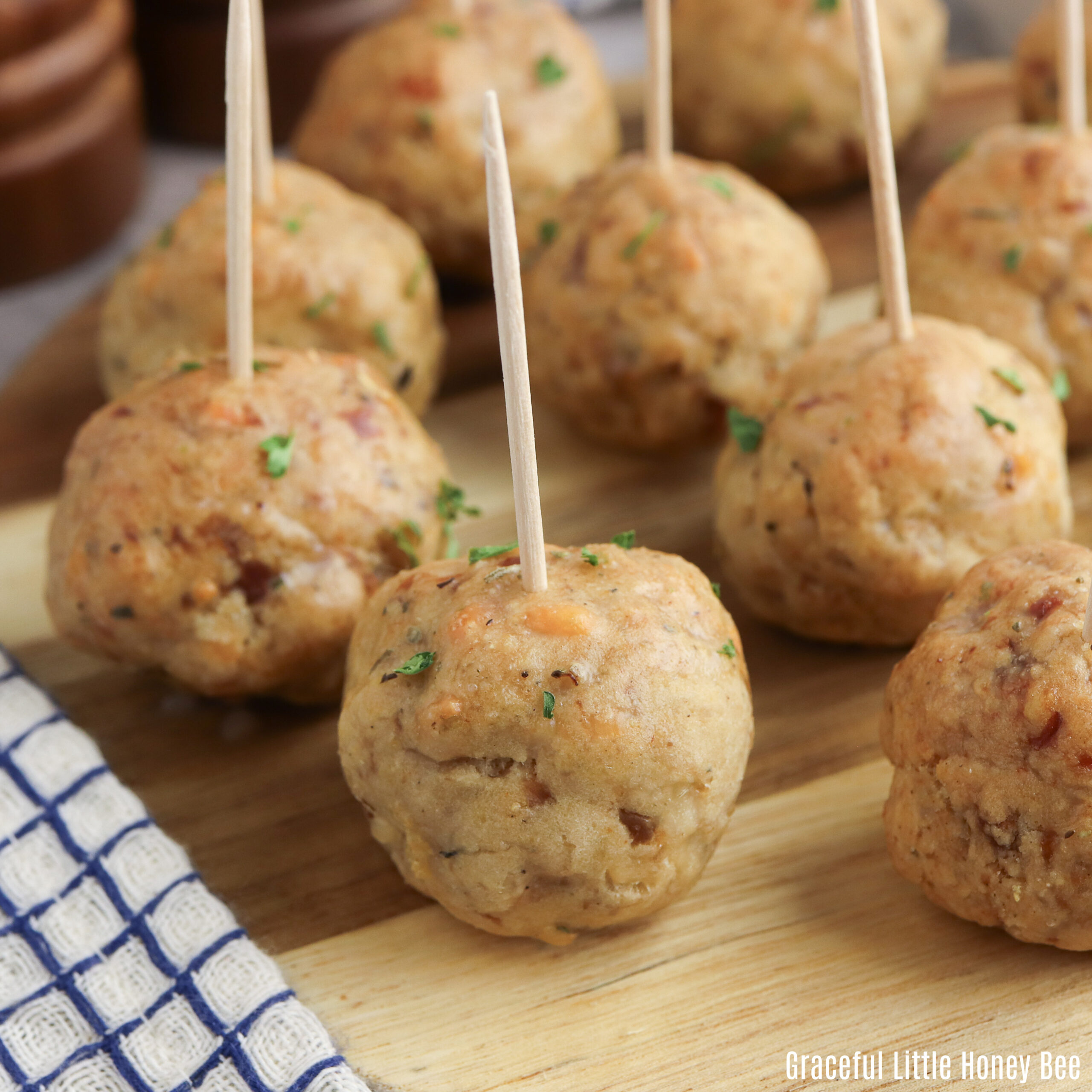 Sausage balls with toothpicks in them on a round wooden plate.